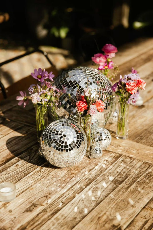 Lot de boules à facettes posées au sol sur parquet. Petits bouquets décoratifs autour.