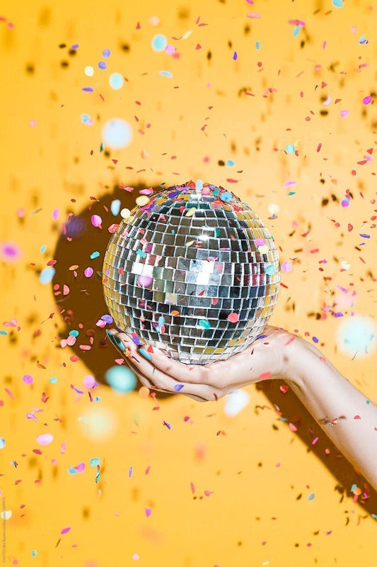Boule à facette 25cm dans la main d'une femme sur fond jaune avec confettis.