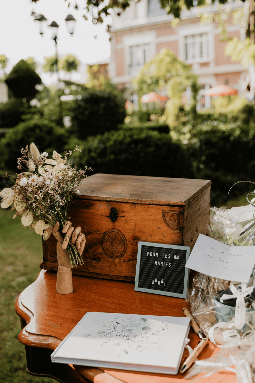 Urne mariage en bois vintage installée sur une table de réception en extérieur avec bouquet de fleurs séchées, livre d'or et décoration champêtre pour mariage bohème.
